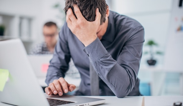 Homme  qui se prend la tête dans la main à son bureau pour représenter les risques psycho-sociaux au travail